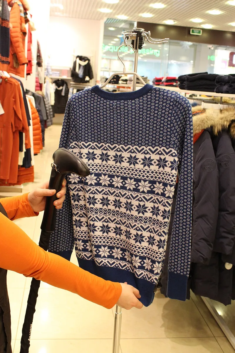 Ein Pullover hängt auf einem Bügel und wird mit einem Hand-Dampfglätter geglättet