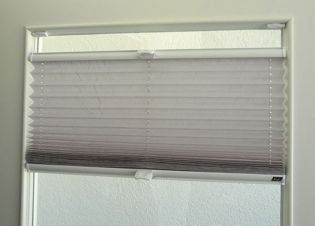 Plissee an einem weißen Kunststofffenster, oben sind die Klemmträger am Fensterflügel zu sehen