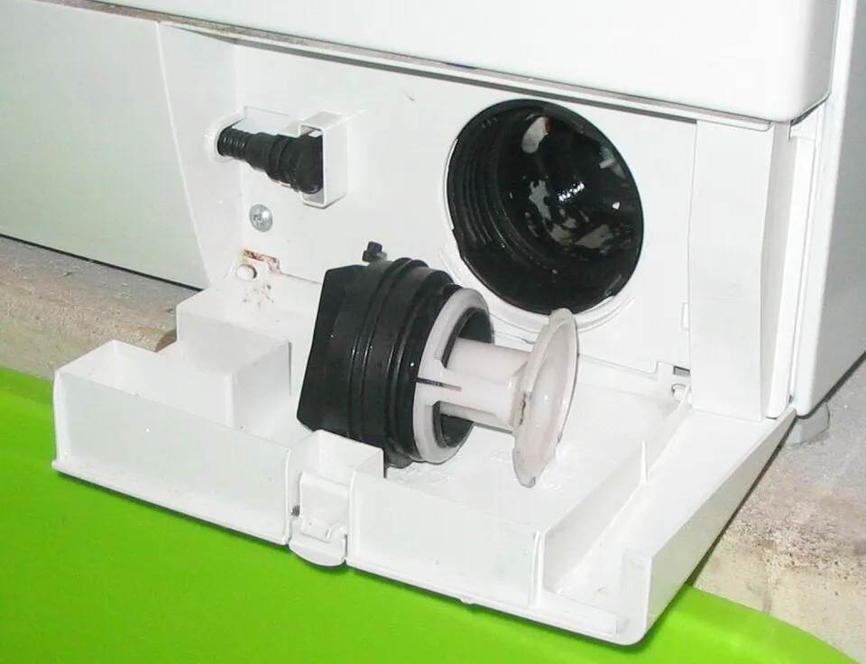 Geöffnete Klappe einer Waschmaschine mit herausgedrehtem Flusensieb